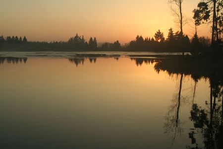 Sunset on a lake. It`s springtime. Calm water and cold weatherの写真素材