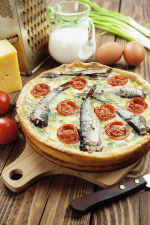 Quiche with sprats and cherry tomatoes on a wooden tableの写真素材