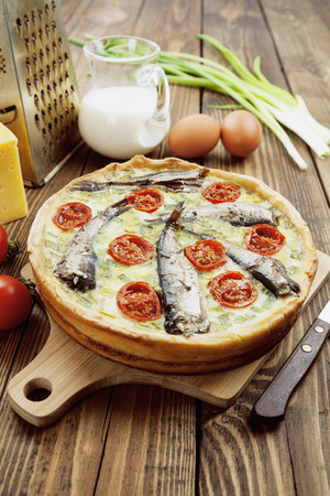 Quiche with sprats and cherry tomatoes on a wooden tableの写真素材