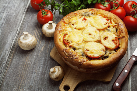 Pie with mushrooms and tomatoes on a wooden tableの写真素材