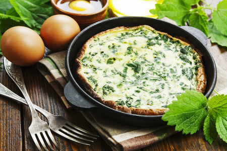 Omelet with nettles in a cast iron pan on a wooden tableの写真素材