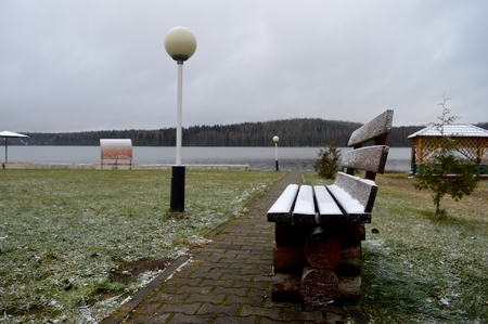 A lonely bench covered with snow on the shore of the lake.の写真素材