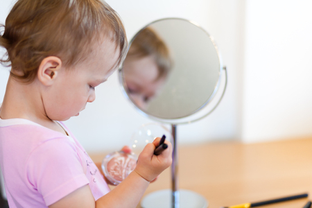 2 years old girl child is doing makeup in front of mirror and using brushの写真素材