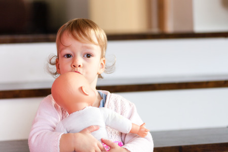 Cute little brown eyes caucasian girl holding and embracing her dollの写真素材