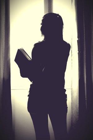 The silhouette of stressed and depressed woman worried about her studies. She look out window. Concept of the need of freedomの写真素材
