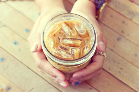Hand holding the glass of iced coffee serving to the customers in vintage styleの写真素材