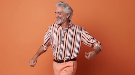 Portrait of happy senior man in striped shirt, dancing on orange backgroundの素材