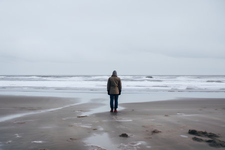 A woman walking on the beach in winter with a cold cloudy dayの素材