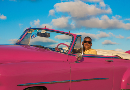 Havana, Cuba, Nov 20, 2017 - Driver sits in a pink Classic American Chevrolet, with sky and clouds...