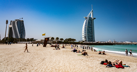 DUBAI, UAE, MAR 20, 2018: Skyscraper shaped like a sail appears to be crashing against skyscraper shaped as a wave across the beachのeditorial素材