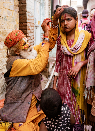 Nandgeon, India, Holi Festival, Feb 25, 2018 - Elderly man paints symbols using gold paint onto the forehead of a womanのeditorial素材