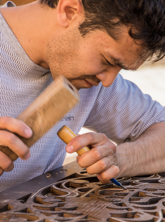 Tashkent, Uzbekistan - May 18, 2017: Man chisels wood engraving in workshop near Chorsu Bazaar