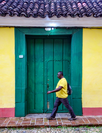 Trinidad, Cuba, Nov 27, 2017 - Man in yellow shirt with motion blur walks past green doorのeditorial素材
