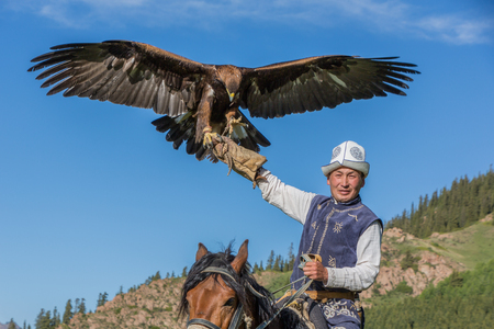 Issyk Kul, Kyrgyzstan - May 29, 2017: Eagle Hunter holds his eagles on horseback, ready to take...