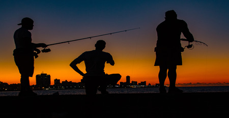 Havana, Cuba, Nov 19, 2017 - Three men seen in silhouette, fishing from the Malecon at sundownのeditorial素材
