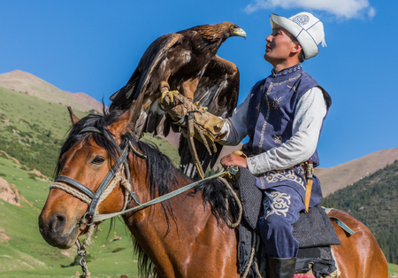 Issyk Kul, Kyrgyzstan - May 29, 2017: Eagle Hunter holds his eagles on horseback, ready to take...