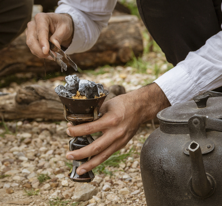 Man tends to hot coals for smoking water pipe tobaccoの写真素材