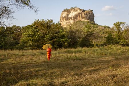 Negombo, Sri Lanka - 2019-03-22 - Monks Walk in Grass Field with Sigiriya Rock in the Background.のeditorial素材