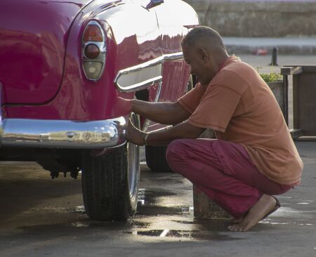 Havana, Cuba Nov 19, 2017 - Man kneels beside car, as he washes his pink classic Chevyのeditorial素材