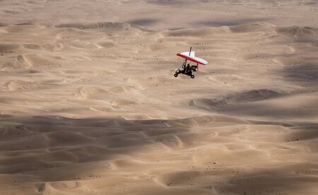 Walvis Bay, Namibia - July 16, 2018: An ultralight aircraft is seen flying with sand dunes as a backdrop in Namibiaのeditorial素材
