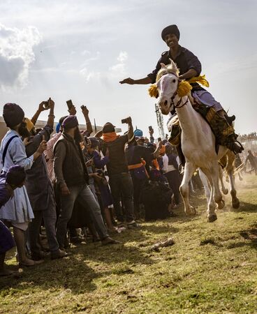 PUNJAB, INDIA, MARCH 2, 2018: Hola Mohalla Festival - Man on horse in full gallop, with all hoofs in the air, races inches past crowdのeditorial素材
