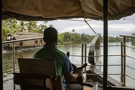 ALLEPPEY, INDIA, MAR 13, 2018: Man drives a houseboat through the backwaters of Keralaのeditorial素材