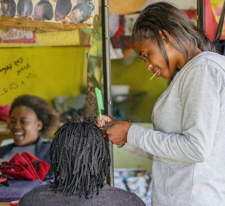 Windhoek, South Africa - July 6, 2018: A hair stylist works on a client s hair in a tiny shop in Namibiaのeditorial素材