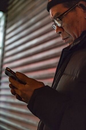 New York City, New York, Feb 14, 2018: Man looks at his smart phone in front of a store grateのeditorial素材
