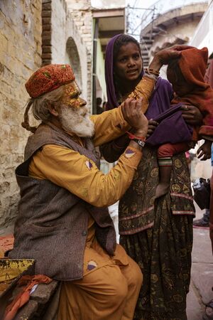 Nandgeon, India, Holi Festival, Feb 25, 2018 - Elderly man paints symbols using gold paint onto the forehead of a womanのeditorial素材