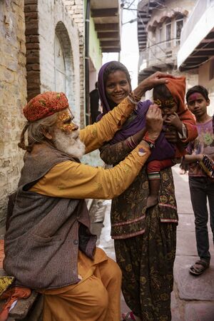 Nandgeon, India, Holi Festival, Feb 25, 2018 - Elderly man paints symbols using gold paint onto the forehead of a womanのeditorial素材