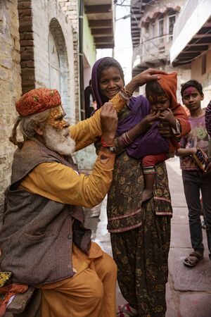 Nandgeon, India, Holi Festival, Feb 25, 2018 - Elderly man paints symbols using gold paint onto the forehead of a womanのeditorial素材
