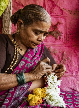 BADAMI, INDIA, MAR 18, 2018: Woman creates flower leis for decorationのeditorial素材