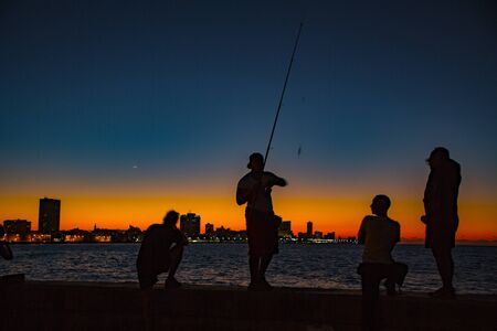 Havana, Cuba - November 19, 2011 - Young men line up on a concrete wall to fish from the bay at sunset in silhouetteのeditorial素材