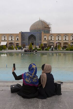Kashan, Iran - 2019-04-14 - Naqshe Cehan Square two women take a selfie beside pond.のeditorial素材
