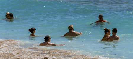 Waikiki, Honolulu, Hawaii - Oct 31, 2021-Adults stand in shallow water just off the beach.