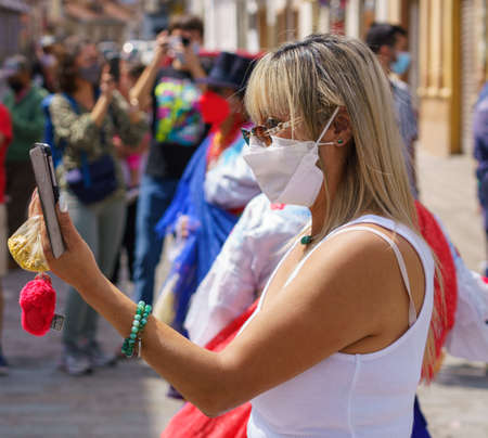 cuenca, Ecuador, Dec 24, 2021 - Woman with COVID mask photographs parade with her phone in the traditional Traveling Child Pase del Nino Christmas Eve Parade.のeditorial素材