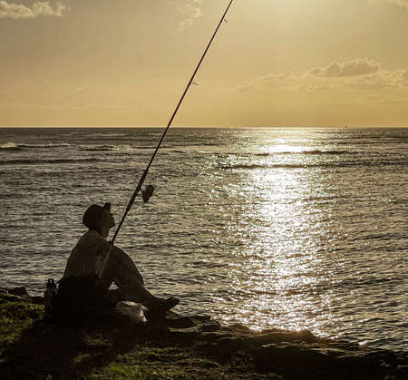 Honolulu, Hawaii - Nov 6, 2021-Silhouette of man fishing from the shore at sunset.の写真素材