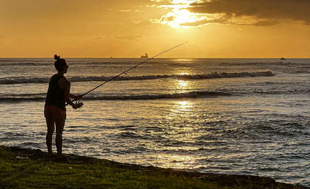 Waikiki, Honolulu, Hawaii - Oct 31, 2021-silhouette of person fishing from the beach at sunset.の写真素材