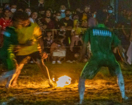 Young men play football (soccer) using a coconut soaked in kerosene and then lit on fire. When the ball breaks apart, a referee replaces it with a newly lit coconut.  The men all play barefoot.の写真素材