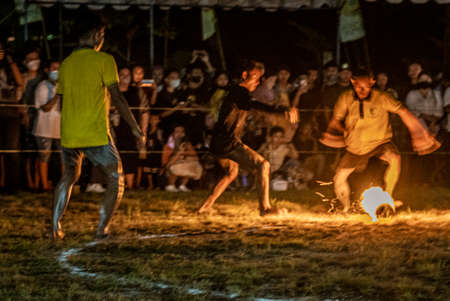 Young men play football (soccer) using a coconut soaked in kerosene and then lit on fire. When the ball breaks apart, a referee replaces it with a newly lit coconut.  The men all play barefoot.の写真素材