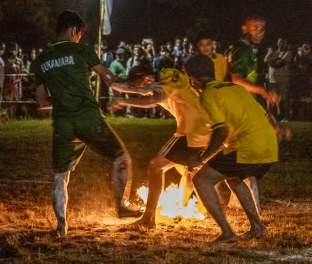 Young men play football (soccer) using a coconut soaked in kerosene and then lit on fire. When the ball breaks apart, a referee replaces it with a newly lit coconut.  The men all play barefoot.の写真素材