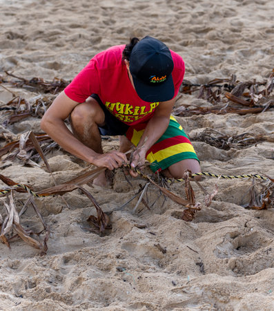 Honolulu, Hawaii/USA - 2022-08-20 - Shaka Filming Hukilau - participant weaves the rope that will hold the fishing nets.のeditorial素材