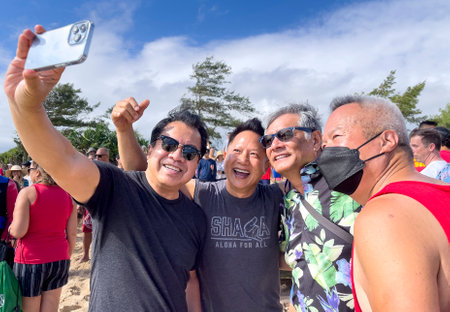 Honolulu, Hawaii/USA - 2022-08-20 - Shaka Filming Hukilau - a group of men take a selfie, one of which is wearing a covid mask.のeditorial素材
