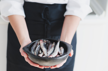 Fresh little fishes in black ceramic bowl over chef's hands.の写真素材