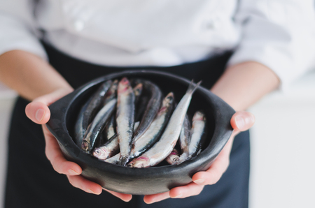 Fresh little fishes in black ceramic bowl over chef's hands.の写真素材