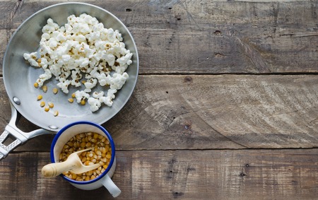 Skillet with popcorn and corn grains on wooden background. Top view.