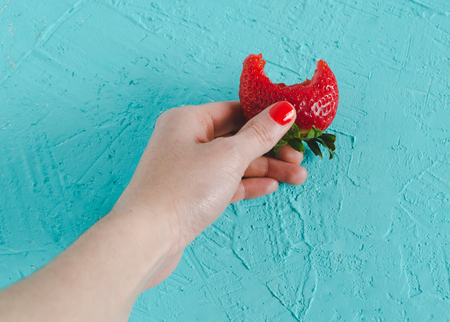 Woman's hand holding a ripe strawberry on blue background. Top view.の写真素材