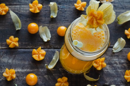 Juice of cape gooseberry in glass cup with scattered cape gooseberries on dark wooden background. Flat lay. Physalisの写真素材