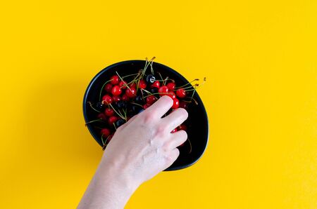 Woman's hand picking cherries from a black bowl. Top view. Copy Space