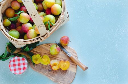 Fresh cut plums on kitchen board and blue background. Wooden basket with whole plums.